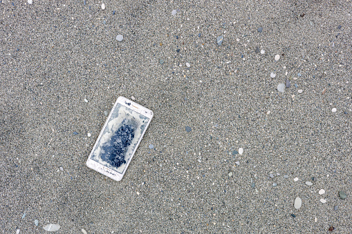 broken lost smartphone on the sand, pollution of the environment with new waste. hazardous waste