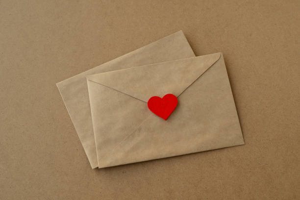 バレンタインデー。クラフト紙の背景にラブレター、封筒、赤いハート。バレンタインカード