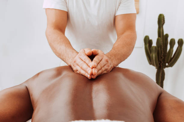 Therapist doing healing treatment on black man's back Black man having back massage in the spa salon after sports. Sports massage. Masseur giving treating massage to his patient with his hands. Muscle recovery after exercise. black male massage stock pictures, royalty-free photos & images