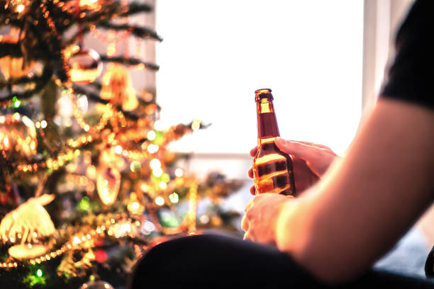 istock Christmas with alcohol and beer bottle. New year's party or Xmas celebration. Drinking problem or alcoholism concept. Craft lager, pilsner or pale ale. Festive tree on winter holiday. 1358026036