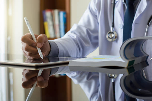 lekarz czytający książkę i praca na cyfrowym tablecie - healthcare and medicine digital tablet medical exam doctor zdjęcia i obrazy z banku zdjęć