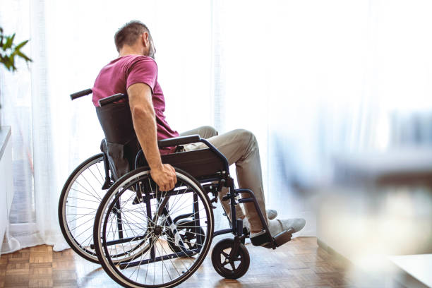 istock Disabled Person Sits in Wheelchair Against Window. 1358029657
