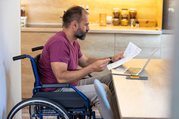 istock Handicapped guy in wheelchair working online from home, using laptop 1358029703