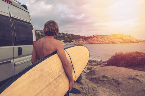 surfer idzie do morza ze swojego kampera zaparkowanego przy plaży - class a motorhome zdjęcia i obrazy z banku zdjęć
