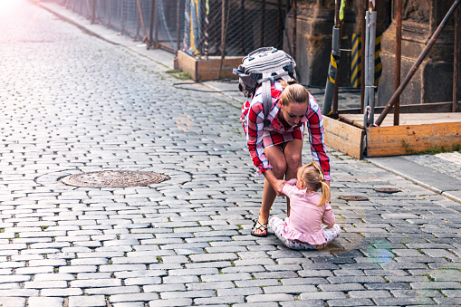 Europe, Czech Republic, Prague, Stare Mesto. - 07/22/2021: A young mother tries to pick up her unruly daughter, who is sitting in the middle of the street.