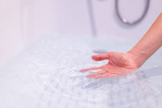 Woman ckecking water temperature in a bath. stock photo