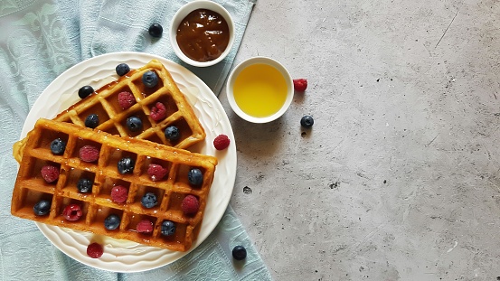 Traditional waffles with fresh raspberries and blueberries on concrete background. Top view, copy space, flat lay .