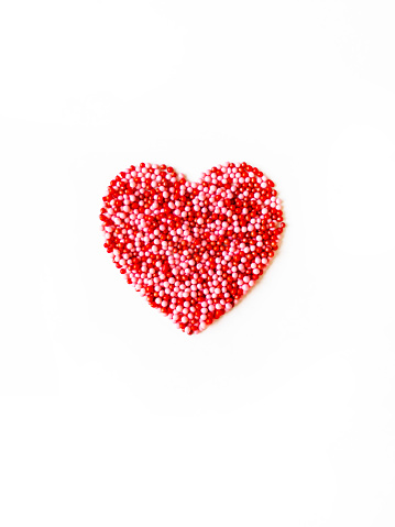 Valentine's card. Love heart made of red and pink pastry sprinkles on white background. Top view. Copy spaace