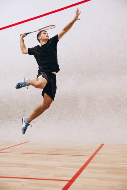 ganzkörperporträt des sportlichen jungentrainings beim squashspielen im sportstudio - racket ball indoors competition stock-fotos und bilder