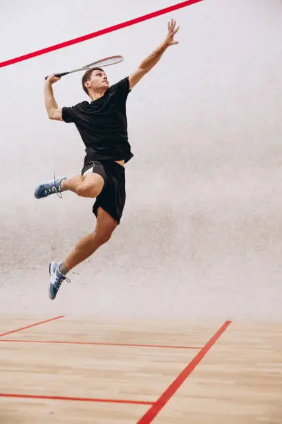 Photo of Full-length portrait of sportive boy training, playing squash in sport studio