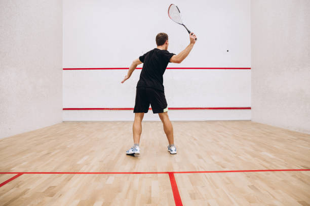 istock Back view of man playing squash game alone in sport studio 1358033611