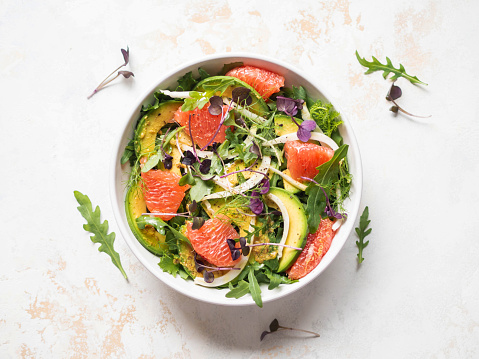 Grapefruit, avocado, arugula, sprouts and fennel salad in white bowl. Top view