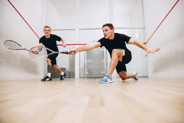 スポーツスタジオの背景の上に孤立したスカッシュをプレイし、一緒に訓練する2人の若いスポーツの男の子のフルレングスの肖像画 - squash racket ストックフォトと画像