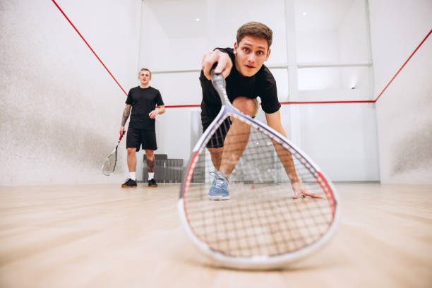 porträt in voller länge von zwei jungen sportlichen jungen, die zusammen trainieren und isoliert über dem hintergrund des sportstudios squash spielen - squash racket stock-fotos und bilder