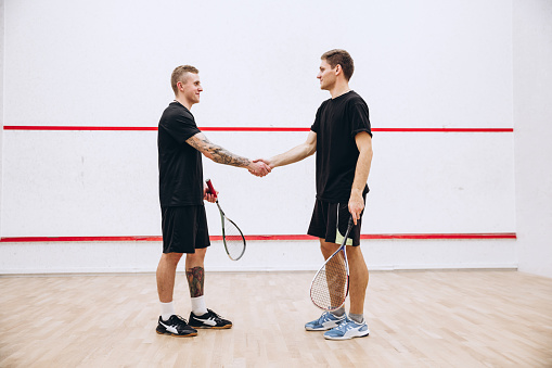 Portrait of two young sportive boys shaking hands, thanking each other after game isolated over studio background. Concept of active life, team game, energy, sport, competition. Copy space for ad