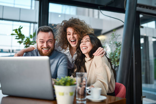 des amis souriants riant de photos amusantes sur un ordinateur portable pendant la pause-café - colleague looking at camera indoors lifestyles photos et images de collection