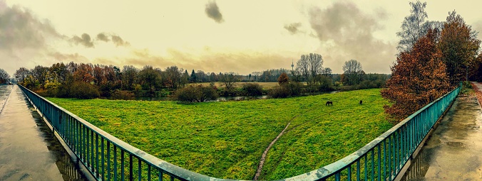 A panoramic picture from a bridge to a field with horses and a river.