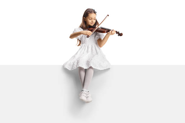 Full length portrait of a girl in a white dress sitting on a blank panel and playing a violin Full length portrait of a girl in a white dress sitting on a blank panel and playing a violin isolated on white background violinist photos stock pictures, royalty-free photos & images