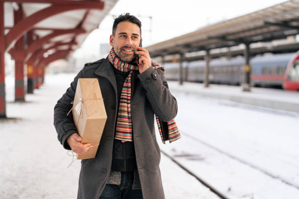 Man with a Christmas gift is waiting at the train station, for a train that will take him home for Christmas. The present is wrapped in brown paper with string ribbon.