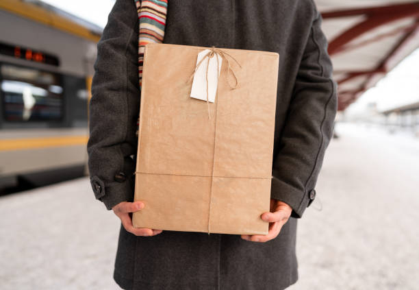 Man with a Christmas gift is waiting at the train station, for a train that will take him home for Christmas. The present is wrapped in brown paper with string ribbon.