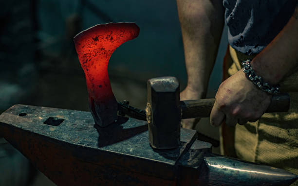 鍛冶屋は、ハンマーで打たれた後、アンビルの赤い熱い斧の遵守をチェックします。鍛冶屋は鍛冶屋で働く - redhot ストックフォトと画像
