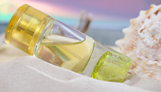 a bottle of bright yellow perfume on a sandy beach next to seashell . light and airy summer fragrances for women. scents for holiday.