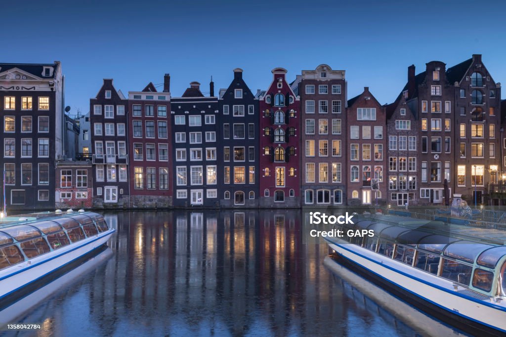 sightseeing boats and canal houses on Damrak in the city centre of Amsterdam at dusk sightseeing boats and canal houses on Damrak in the city centre of Amsterdam; Amsterdam, Netherlands Amsterdam Stock Photo