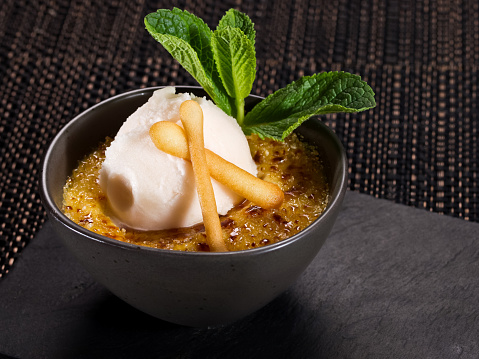 sweet dessert creme brulee with scoop of ice cream, served in a small ceramic bowl on a stone plate, horizontal photo on dark background