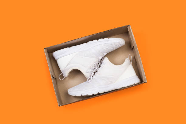 istock A pair of white sneakers in a box on a orange backgound 1358047541