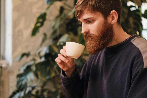 istock Young attractive bearded man drinking coffee resting in cafe alone 1358047848