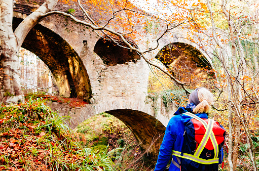 Woman looking at Craigmin Bridge over the Burn of Letterfourie 4km south of the town of Buckie on the North Sea coast of Moray, Scotland. This is an 18th century stone construction with an unusual two tier design of circular arches and internal mural passage.