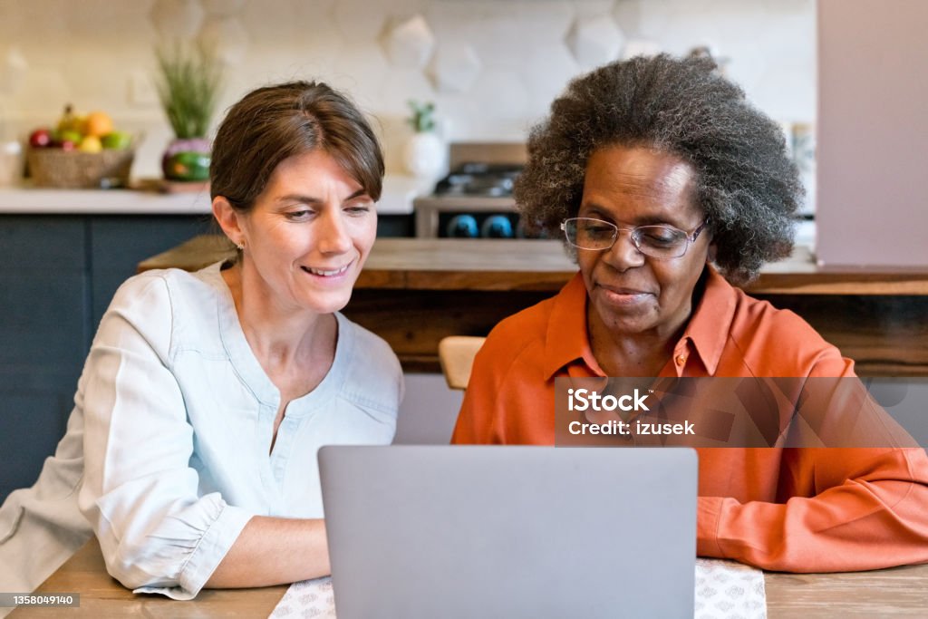 Healthcare worker teaching laptop to senior woman Caregiver teaching laptop to senior woman. Elderly female is wearing eyeglasses. They are at home. Community Outreach Stock Photo
