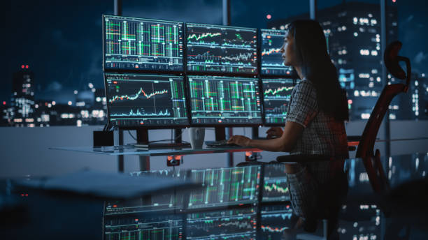istock Financial Analyst Working on a Computer with Multi-Monitor Workstation with Real-Time Stocks, Commodities and Exchange Market Charts. Businesswoman Drnking Coffee at Work in Investment Bank Office. 1358049217