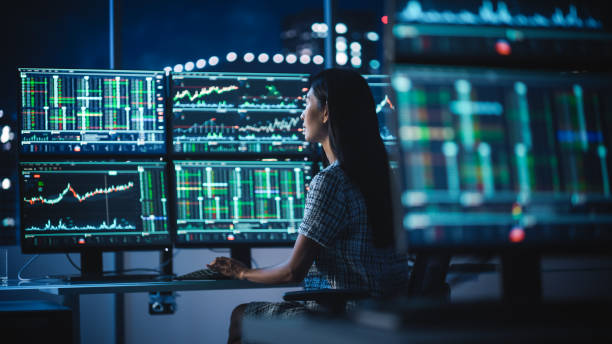 istock Financial Analyst Working on a Computer with Multi-Monitor Workstation with Real-Time Stocks, Commodities and Exchange Market Charts. Businesswoman at Work in Investment Broker Agency Office at Night. 1358049717