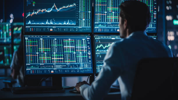 istock Financial Analysts and Day Traders Working on a Computers with Multi-Monitor Workstations with Real-Time Stocks, Commodities and Exchange Market Charts. Team of Brokers at Work in Agency. 1358049775