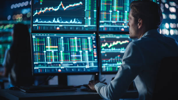 istock Financial Analyst Working on a Computer with Multi-Monitor Workstation with Real-Time Stocks, Commodities and Foreign Exchange Charts. Businessman Works in Investment Bank City Office at Night. 1358049785