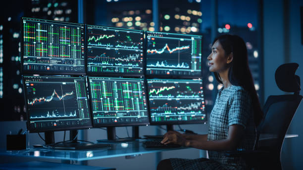 istock Financial Analyst Working on a Computer with Multi-Monitor Workstation with Real-Time Stocks, Commodities and Exchange Market Charts. Businesswoman at Work in Investment Broker Agency Office at Night. 1358049795