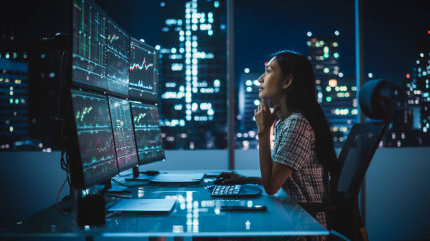 portrait of a financial analyst working on computer with multi-monitor workstation with real-time stocks, commodities and exchange market charts. businesswoman at work in investment broker agency. - 證券交易市場 個照片及圖片檔