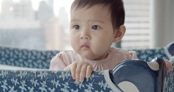 cute innocent baby girl enjoys playing on a playpen at home. - babybox stockfoto's en -beelden