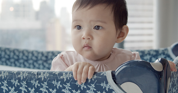 South east Asian Cute innocent baby girl enjoys playing on a playpen at home. love care concept.