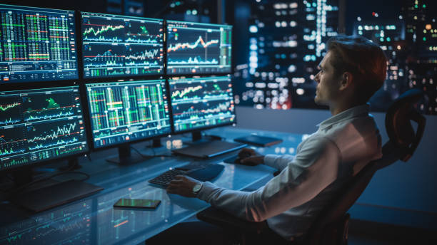 istock Financial Analyst Working on a Computer with Multi-Monitor Workstation with Real-Time Stocks, Commodities and Foreign Exchange Charts. Businessman Works in Investment Bank City Office Late Evening. 1358050084