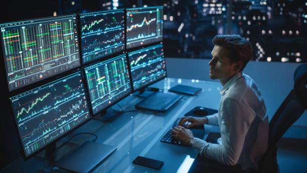 Financial Analyst Working on a Computer with Multi-Monitor Workstation with Real-Time Stocks, Commodities and Foreign Exchange Charts. Businessman Works in Investment Bank City Office Late Evening. analista financiero que trabaja en una computadora con estación de trabajo de múltiples monitores con acciones, materias primas y gráficos de divisas en tiempo real. empresario trabaja en la oficina del banco de inversión de la ciudad a última hora de