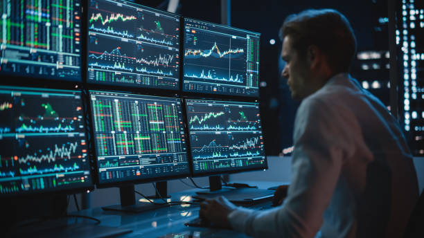 analista finanziario che lavora su un computer con workstation multi-monitor con azioni in tempo reale, materie prime e grafici di mercato di scambio. l'uomo d'affari lavora nell'ufficio di investment bank downtown di notte. - quotazione di borsa foto e immagini stock