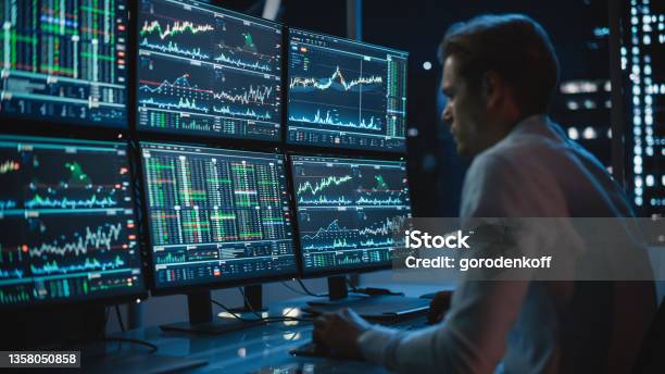Financial Analyst Working On A Computer With Multimonitor Workstation With Realtime Stocks Commodities And Exchange Market Charts Businessman Works In Investment Bank Downtown Office At Night Stock Photo - Download Image Now