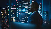 istock Successful Businessman Looking Out of the Window on Late Evening. Modern Hedge Fund Investor Enjoying Successful Life. Urban View with Down Town Street with Skyscrapers at Night with Neon Lights. 1358050964
