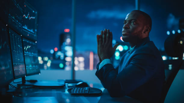 Financial Analyst Working on Computer with Multi-Monitor Workstation with Real-Time Stocks, Commodities and Exchange Market Charts. African American Trader Works in Investment Bank Late at Night. Financial Analyst Working on Computer with Multi-Monitor Workstation with Real-Time Stocks, Commodities and Exchange Market Charts. African American Trader Works in Investment Bank Late at Night. stock brokers stock pictures, royalty-free photos & images