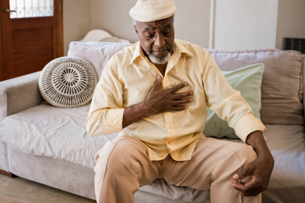 Elderly man having pain in chest at home Senior man suffering from pain in chest. Elderly male is having heart attack. He is sitting on sofa. chest pain stock pictures, royalty-free photos & images