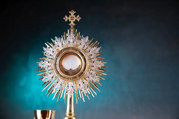 Catholic symbols composition: monstrance, The Cross, Holy Bible, rosary and golden chalice.