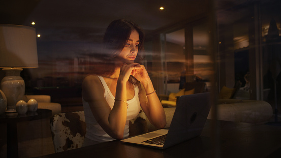 Businesswoman working late from home. Looking through window