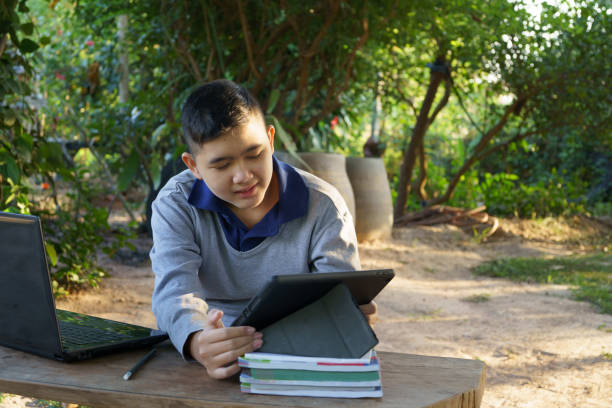istock Boy is studying online on a wooden table with a laptop computer and tablet during morning hours in a rural home. concept online education countryside area and work from home 1358052647